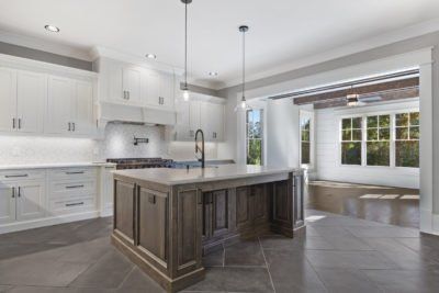 Spacious, light-filled kitchen with white cabinets, gray island, and an open doorway to a windowed alcove.