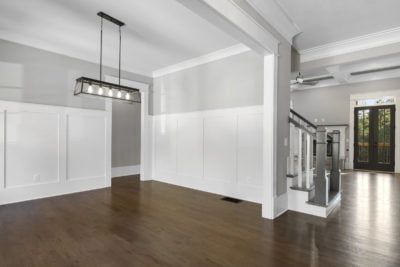 Empty dining room with dark wood floors, white wainscoting, and a modern light fixture.
