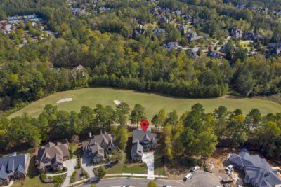 Aerial view of a house with a red pin, surrounded by trees and a golf course.