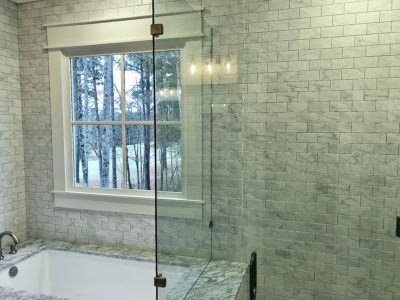 Bathroom with white brick tile, window overlooking trees, and glass shower door.