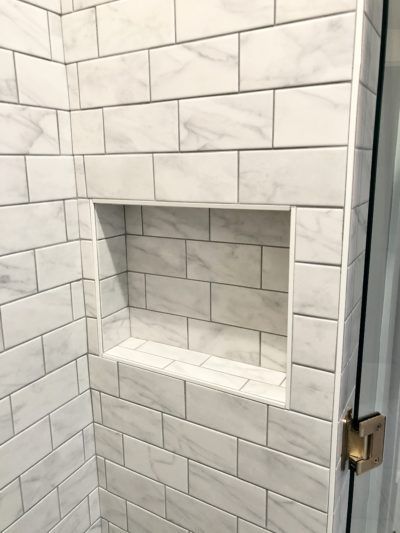Shower with marble-look tile and a built-in rectangular shelf.