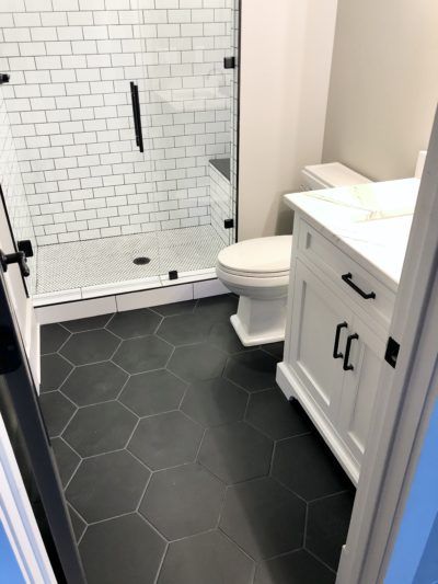 Bathroom with white cabinetry, black hexagonal floor tiles, and a white subway tile shower.