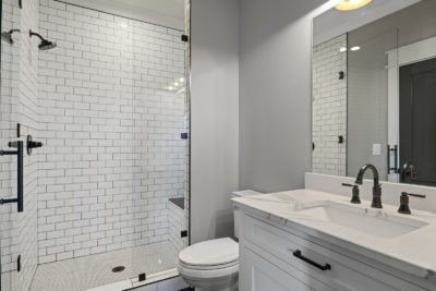 Bathroom with white subway tile shower, glass door, white vanity, gray walls, and black fixtures.