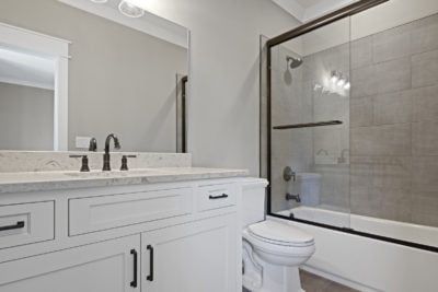 Bathroom with white vanity, black hardware, glass shower, and gray walls.