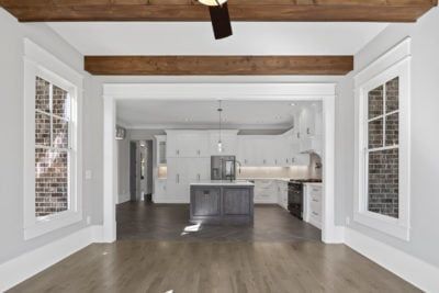 Interior view of a modern home, with a dining area looking into a kitchen. Features exposed wood beams and white cabinetry.