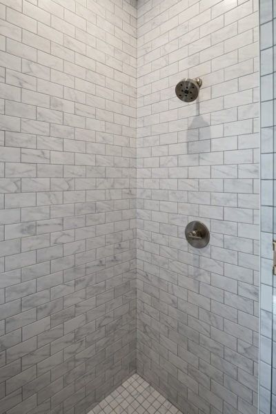 Shower stall with white marble subway tile and silver shower fixtures.