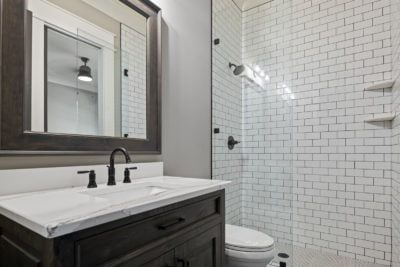 Bathroom with dark wood vanity, white countertop, and white subway tile shower.