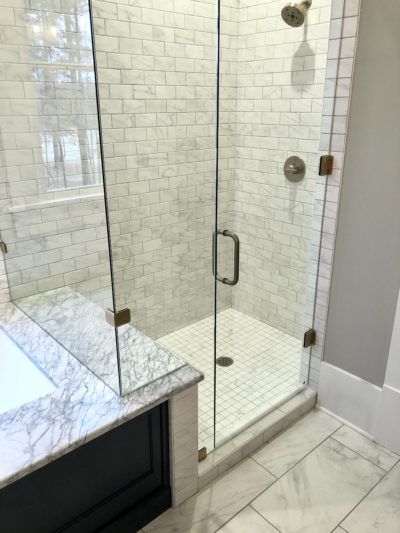 Glass shower enclosure with white tile and marble vanity.