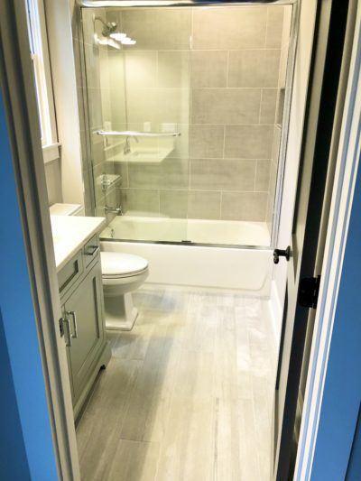Bathroom with gray tile, shower, toilet, and vanity seen through a doorway.
