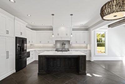 Bright white kitchen with dark island and appliances. Light pendants hang above the island.