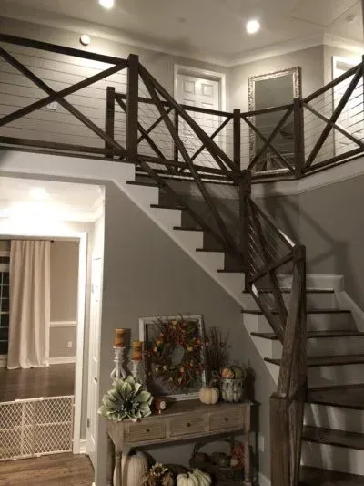 Wooden staircase with decorative railing, leading to a second-floor landing. The entry area is decorated for fall.