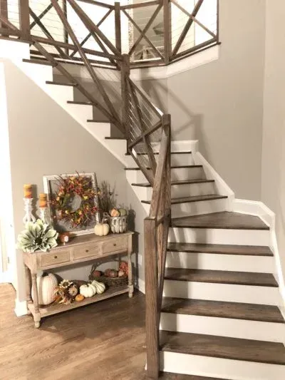 Wooden staircase with white risers, autumnal decor on console table.