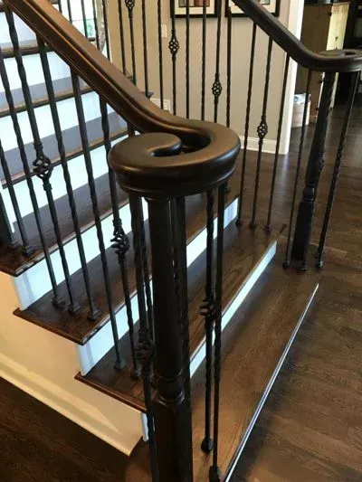 Wooden staircase with dark brown handrail and wrought iron spindles.