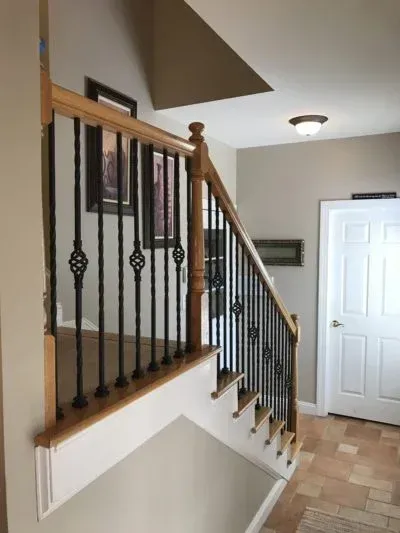Staircase with wooden handrail, black spindles, and neutral walls leading to a white door.