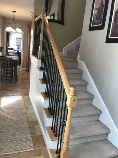 Staircase with light wood handrail, black spindles, and carpeted stairs, leading up to the second floor.