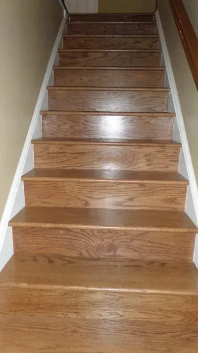 Wooden stairs with white risers and a beige wall.