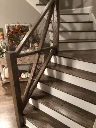 Wooden staircase with dark brown treads, white risers, and a wooden handrail with cable railing.