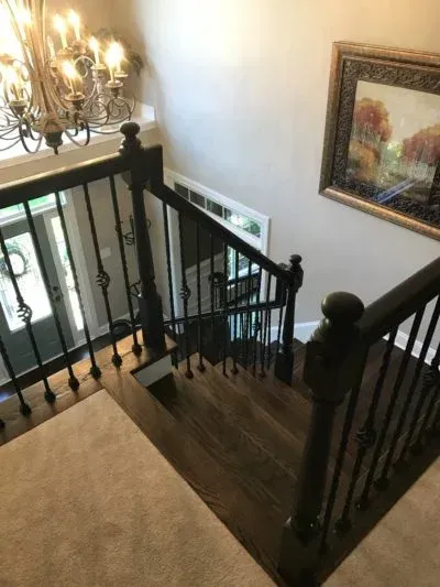 Staircase with dark wooden steps and railings, ornate iron balusters, chandelier, and artwork on a wall.
