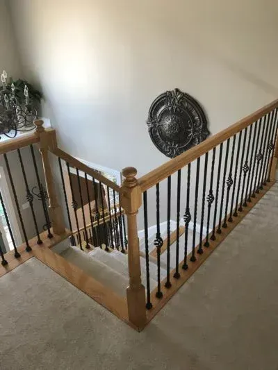 Staircase with oak railing and black iron balusters, descending from an upper level with beige carpet.