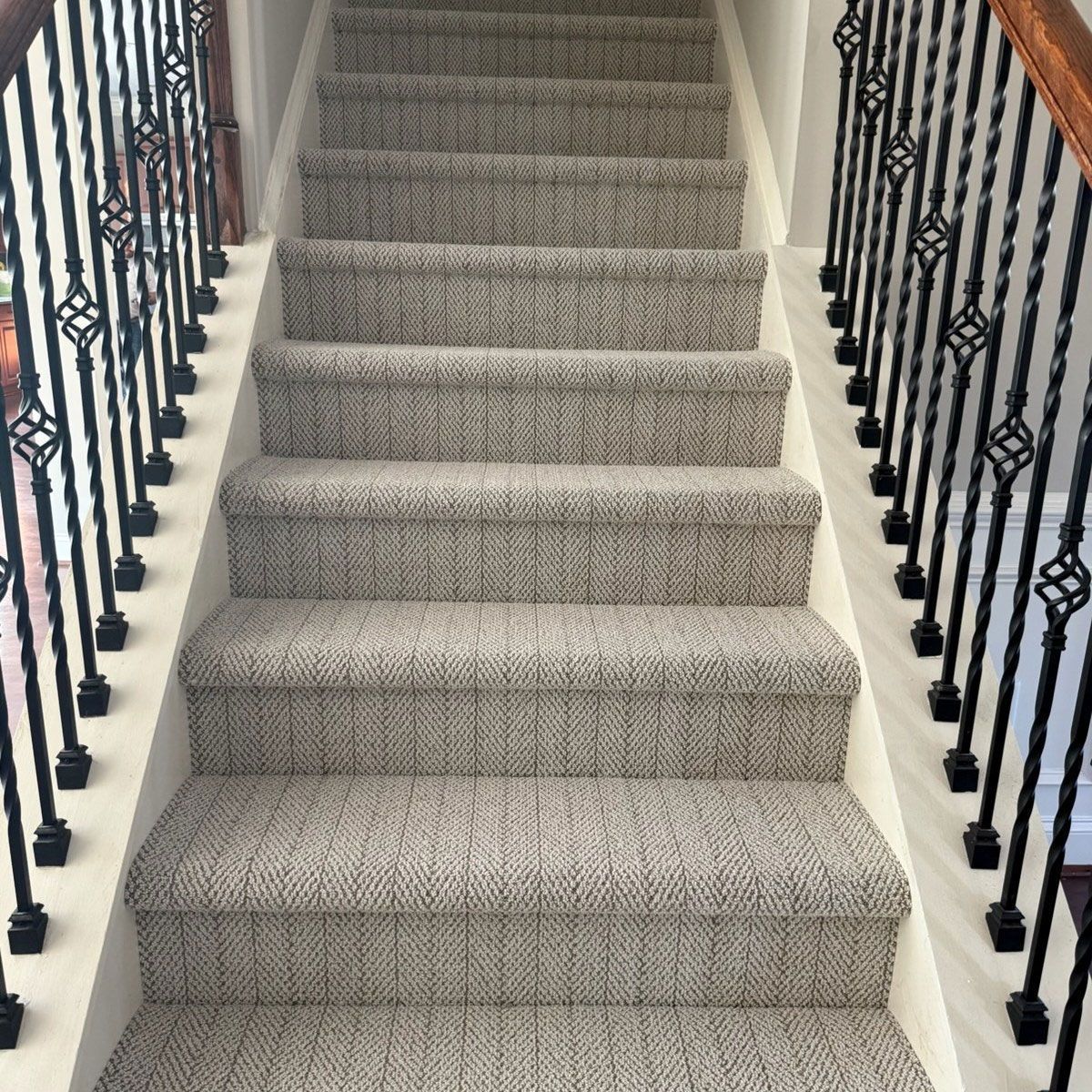 Staircase with gray patterned carpet, flanked by black iron railings and white trim.
