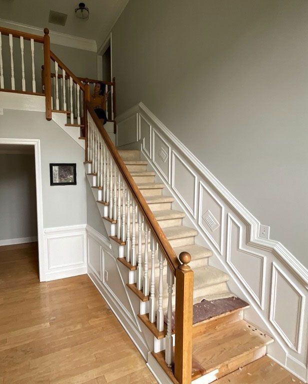 Interior view of a staircase with light-colored walls and a wooden railing. Stair treads have partial carpet.