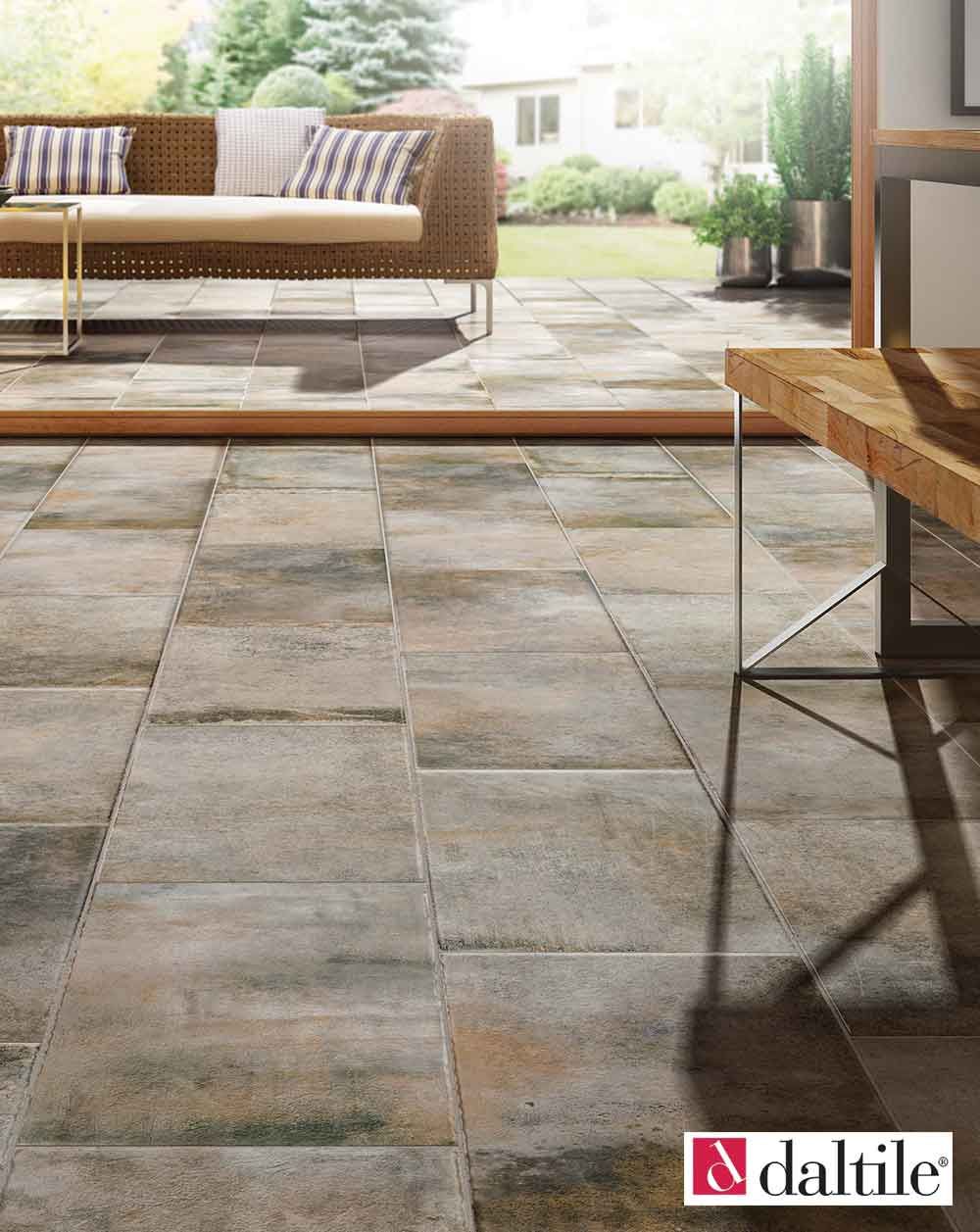 Outdoor patio with brown, rectangular tiles, a rattan sofa, and a wooden table.
