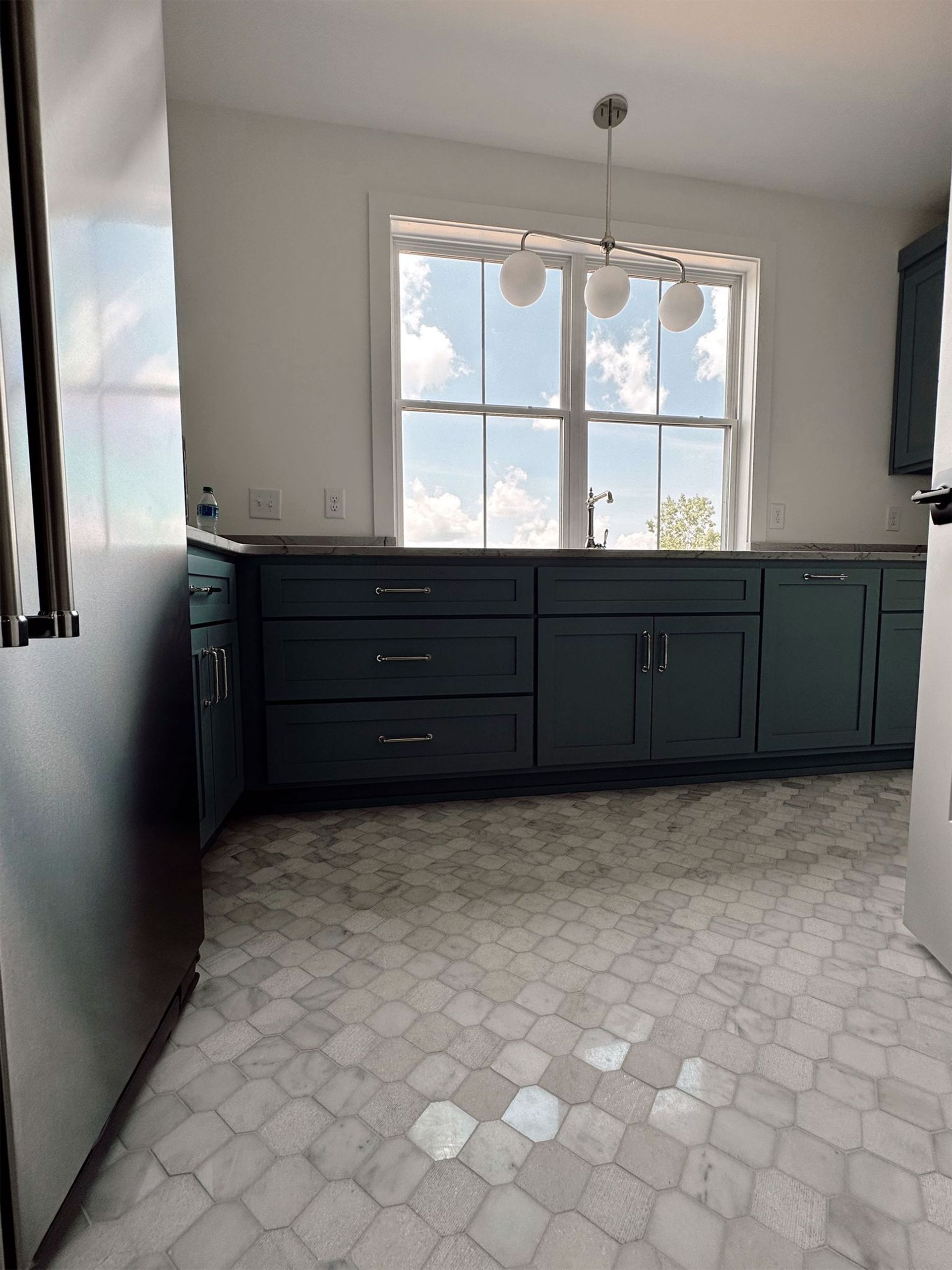 Kitchen with teal cabinets, window, pendant lights, and patterned tile floor.