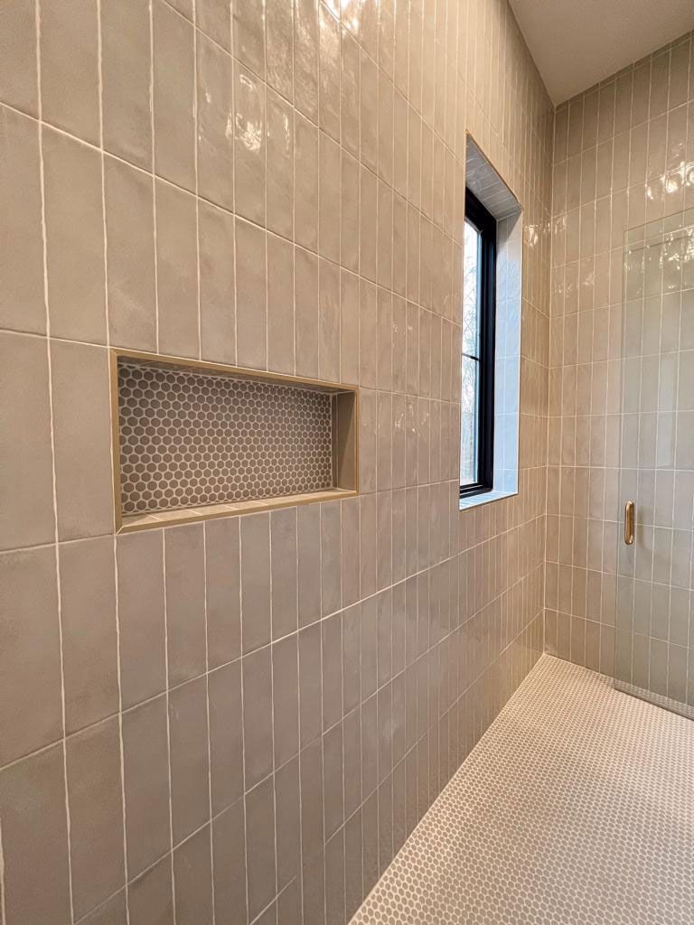 Bathroom with rectangular tiles on walls, niche with patterned tiles, small window, and light-colored floor.