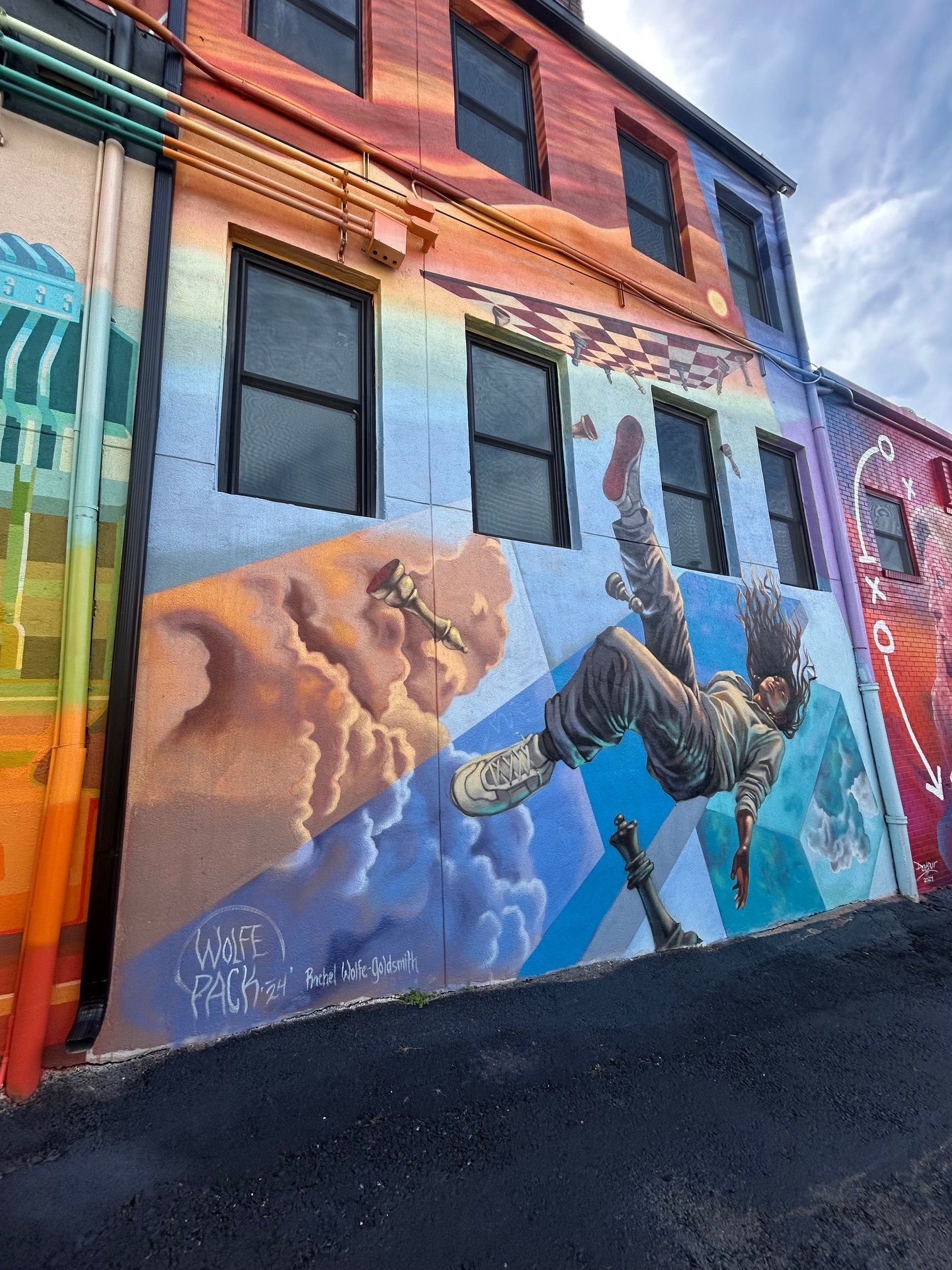 Colorful building with a mural of a person falling through a cloudy sky. The building's side is painted with a rainbow gradient.