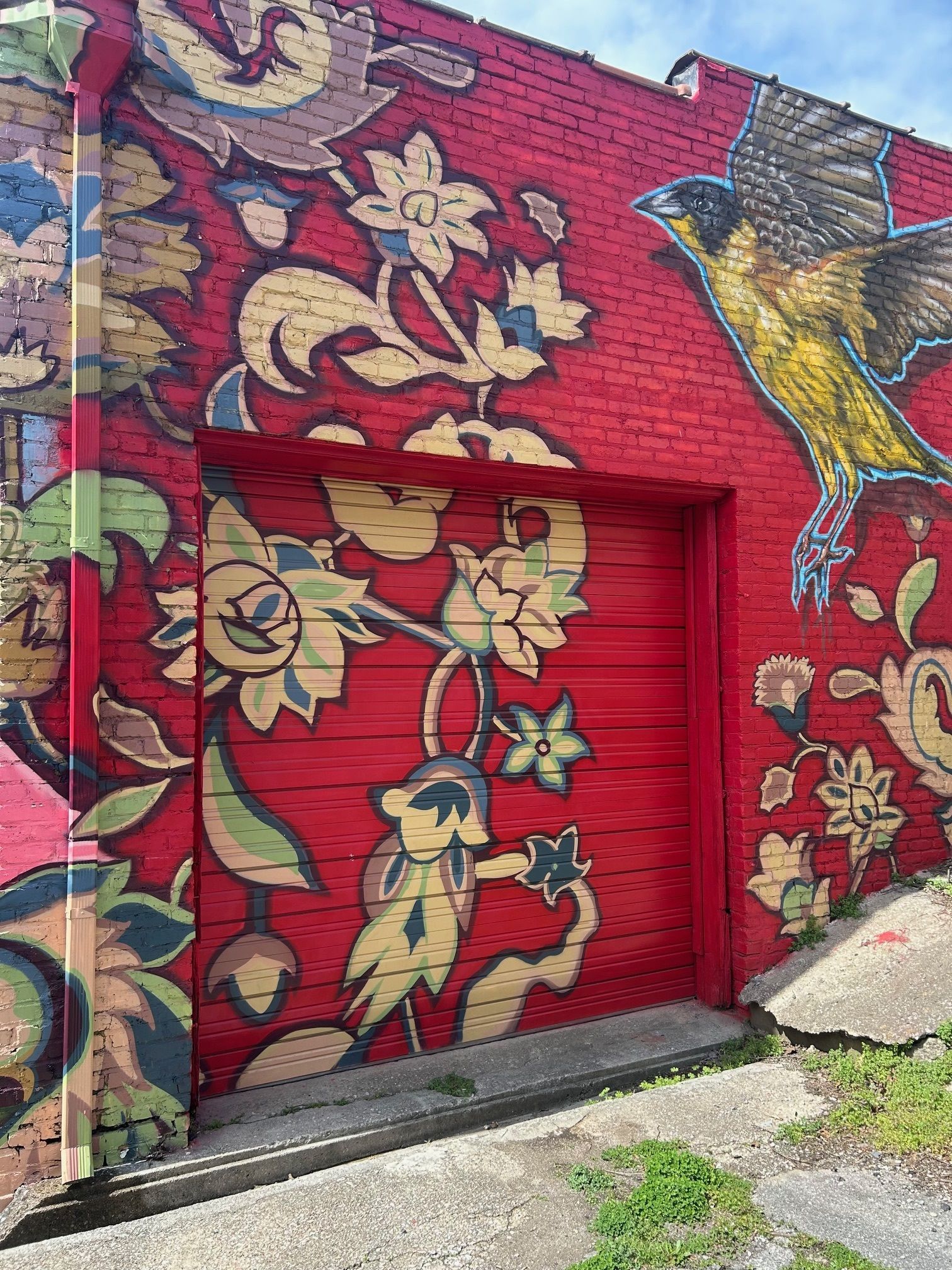 Red brick wall mural with floral designs and a yellow bird. Includes a red door that blends with the mural.