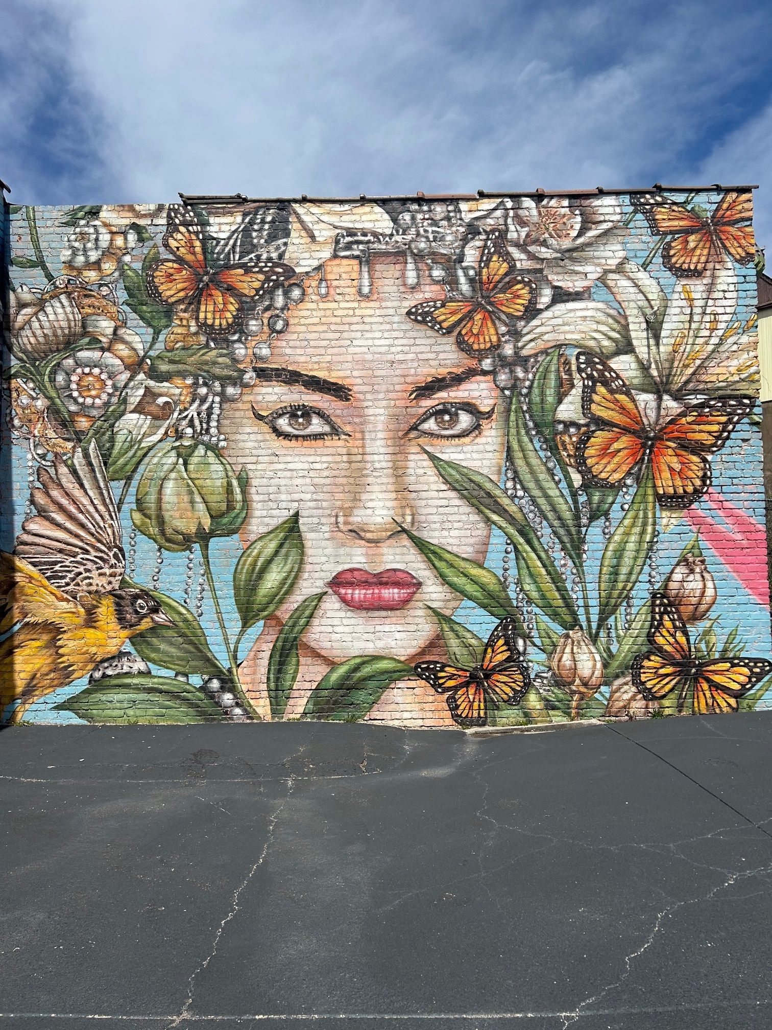 Mural of a woman's face surrounded by flowers and monarch butterflies against a blue sky.