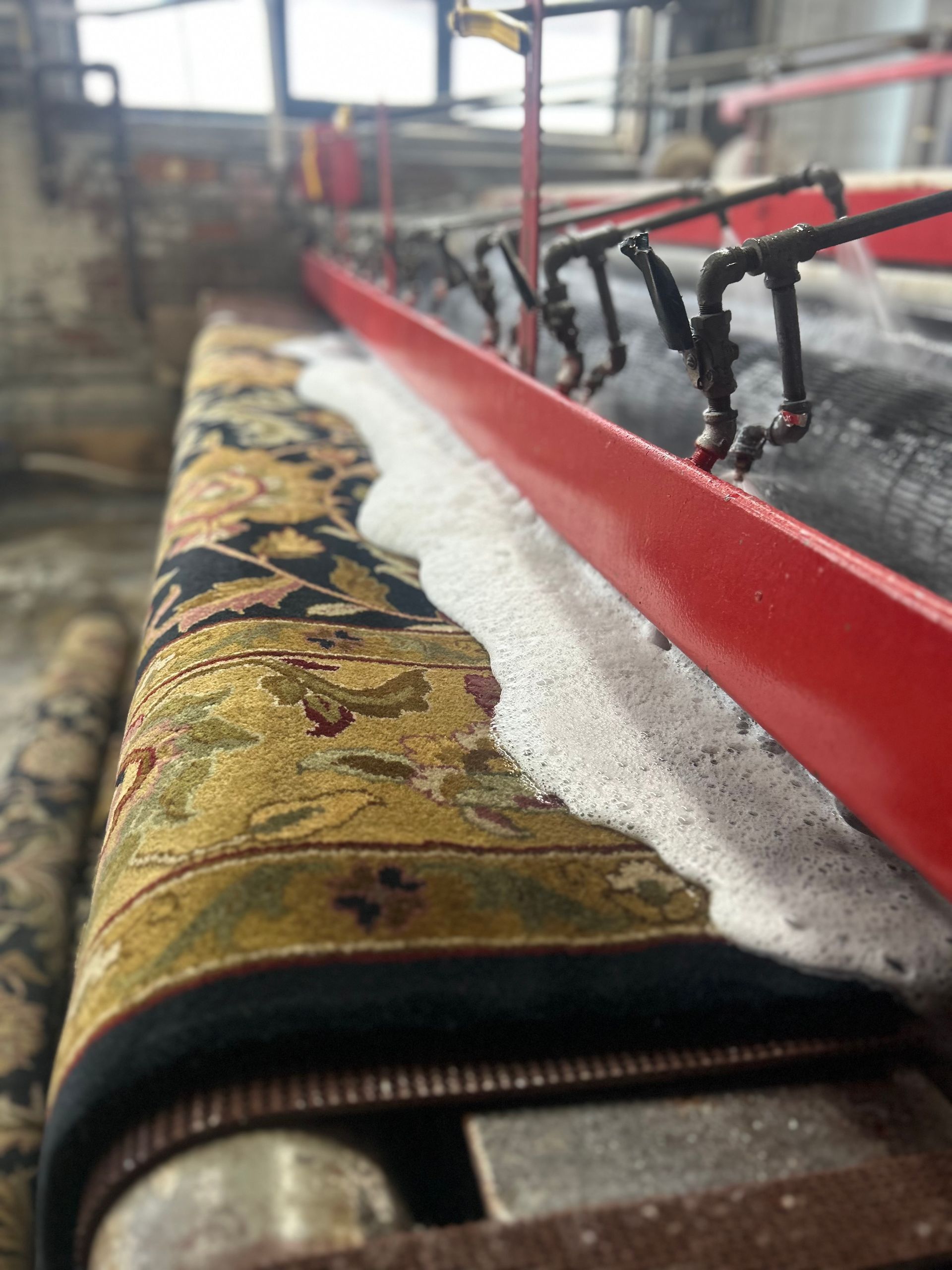 Rug being cleaned by an automated machine, soap bubbles covering its surface.