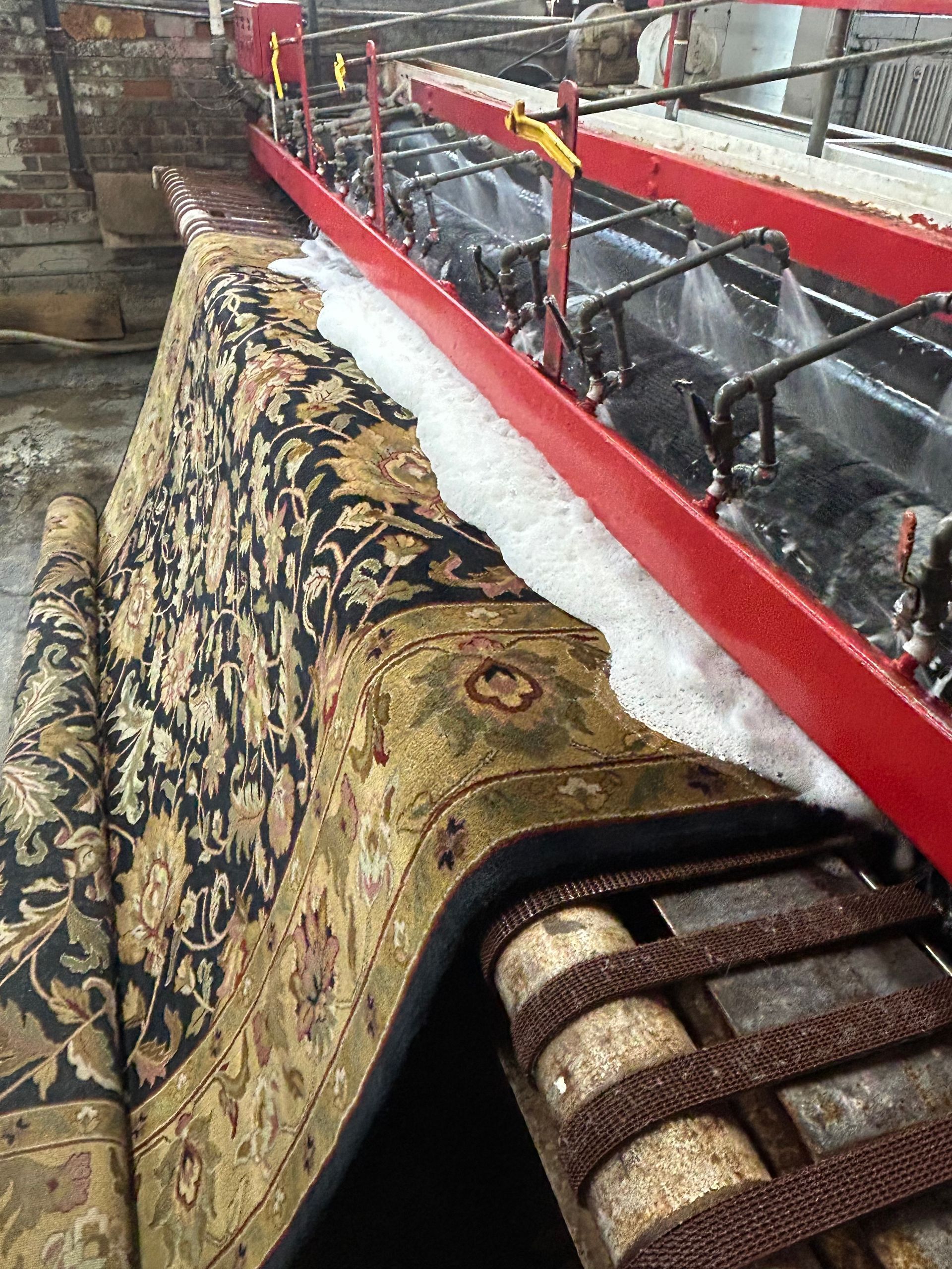 Rug being cleaned in an industrial washing machine. Soap and water flow on the patterned rug.
