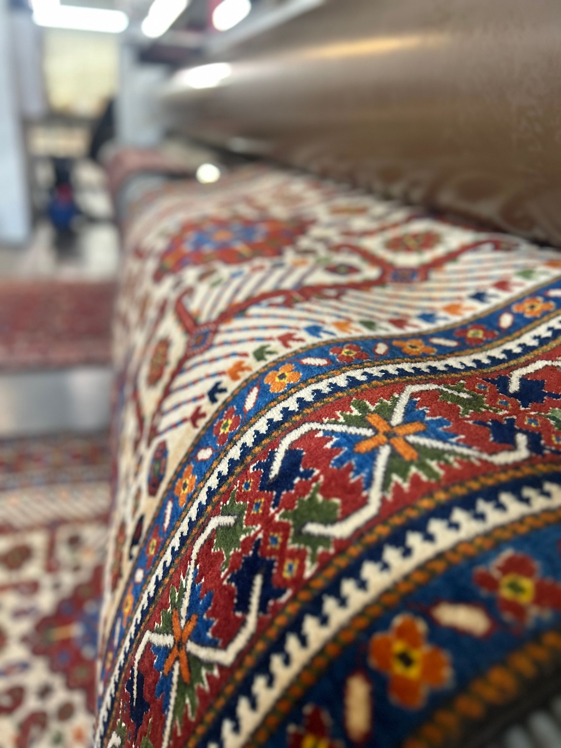 Rolled-up ornate rug with red, blue, and white patterns, being pressed by a machine.