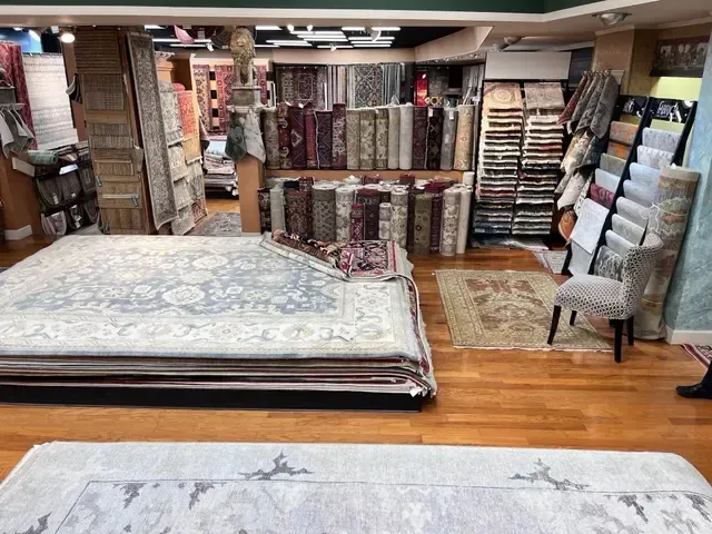 Interior of a carpet store, showing many rolled and folded rugs of various colors and patterns on wooden floors.