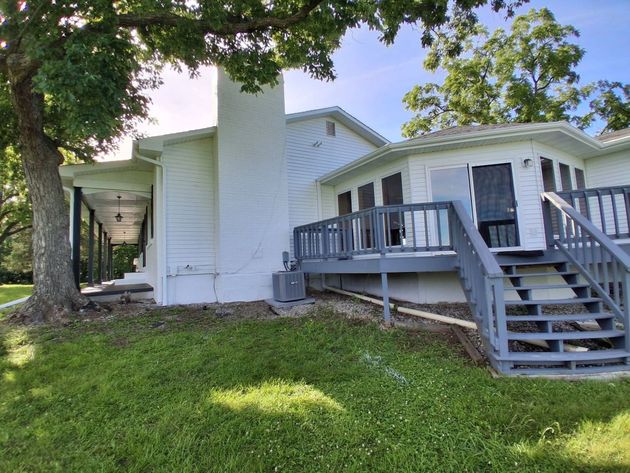 White house with front porch, steps, and railings on a grassy hillside under trees.