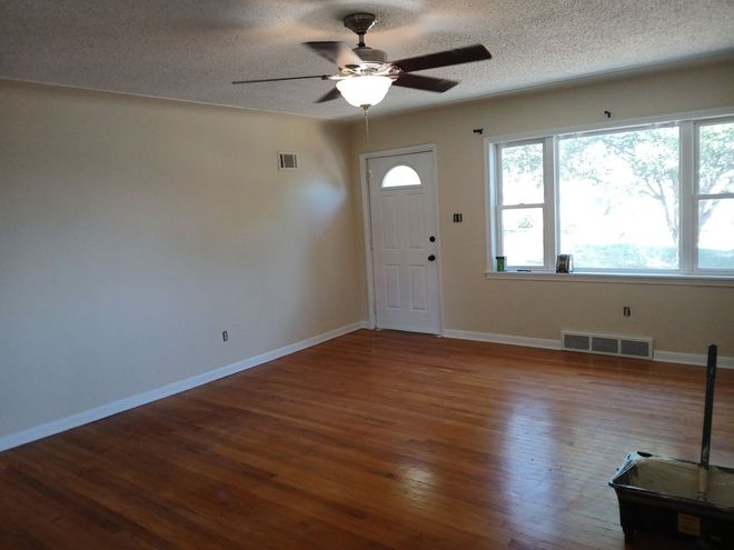 Empty beige bedroom with carpet, window blinds, and ceiling fan in the corner.