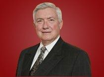 Portrait of a man in a dark suit and patterned tie against a red background