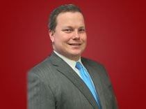 Man in a gray suit and blue tie posing against a red background