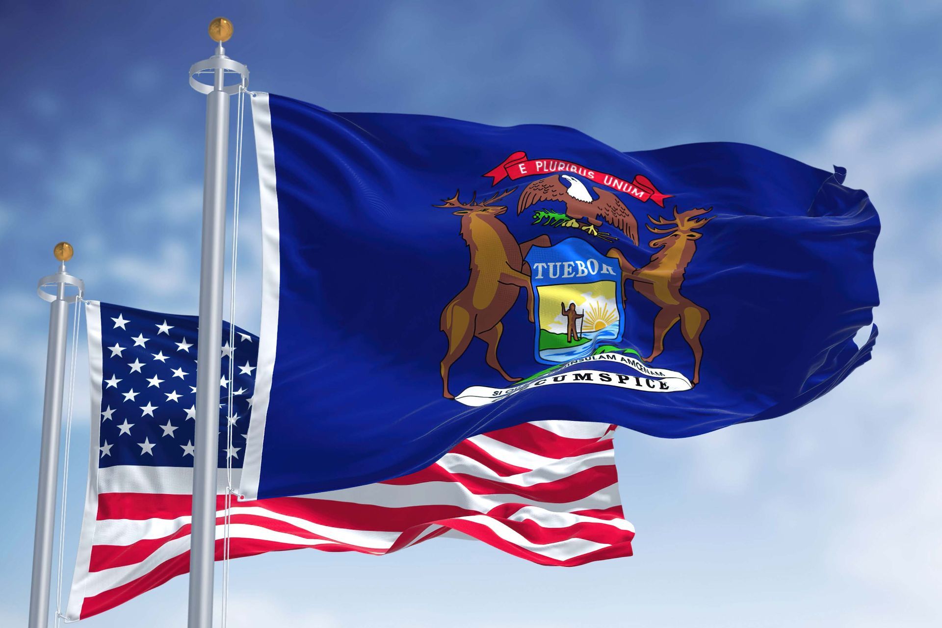 U.S. and Michigan flags waving on flagpoles against a blue sky