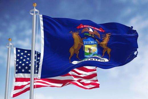 U.S. and Michigan flags waving on flagpoles against a blue sky