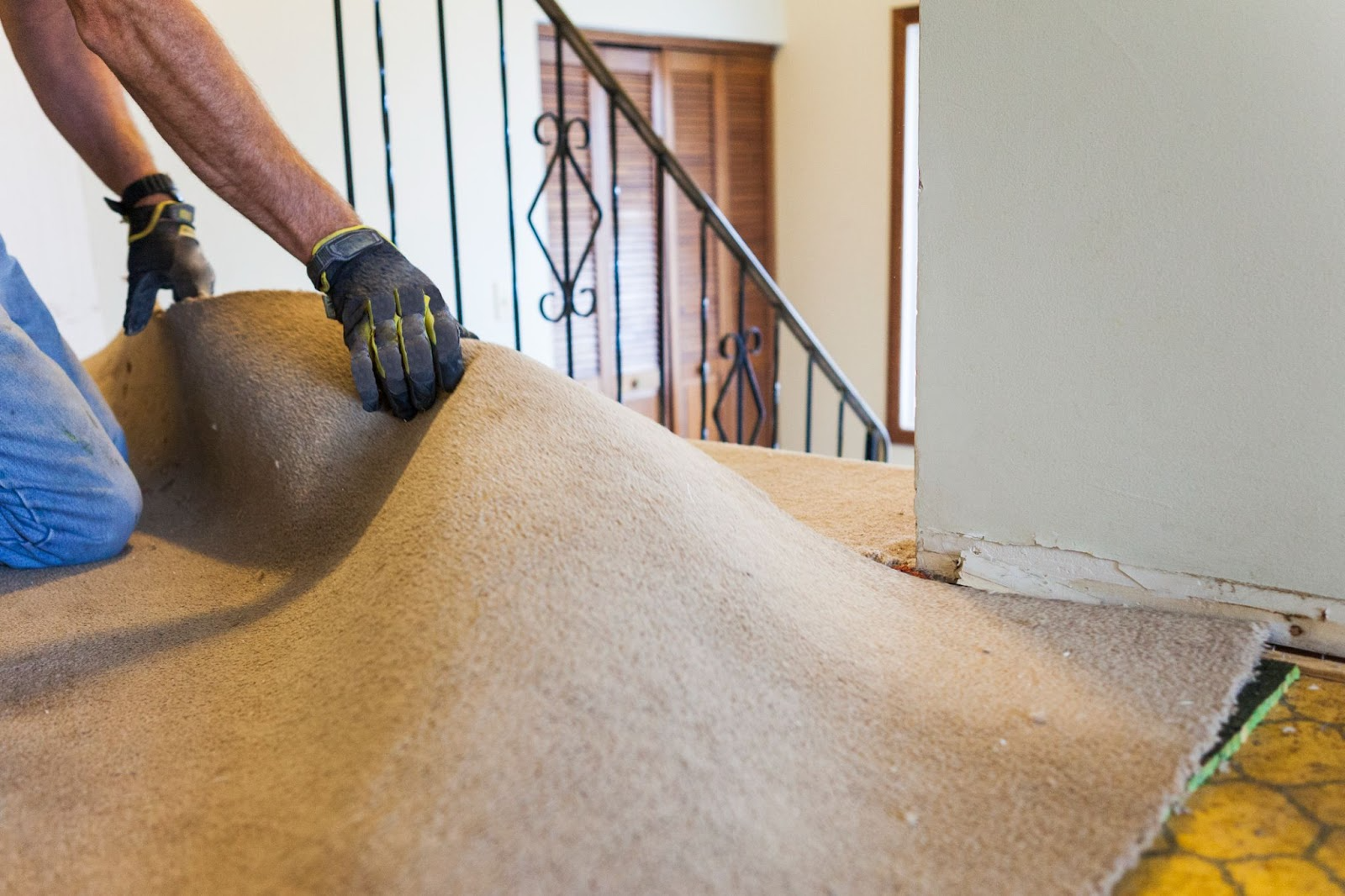 Person kneeling, installing beige carpet on a staircase landing.