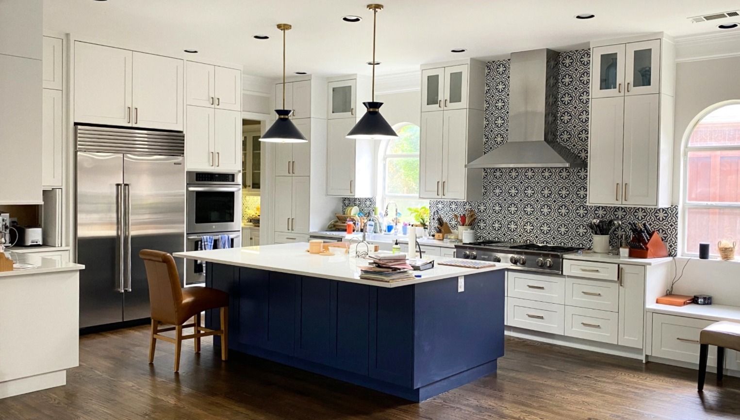 Bright kitchen with white cabinets, blue island, stainless steel appliances, and mosaic backsplash.