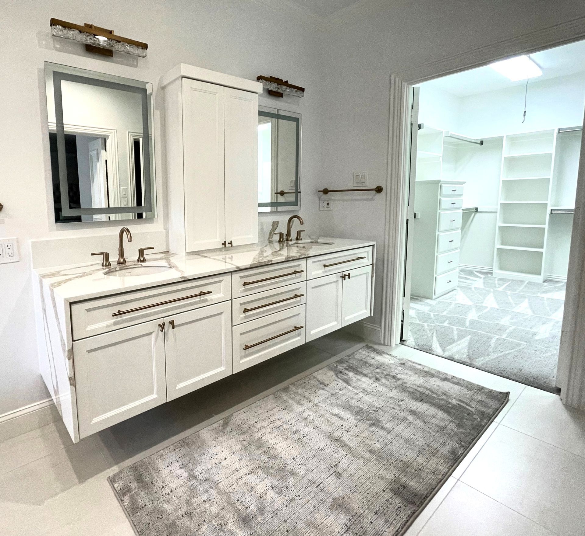 White bathroom with floating vanity, two mirrors, and walk-in closet in the background.