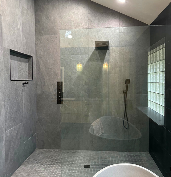 Modern gray tiled bathroom with glass shower door, black fixtures, and mosaic floor.