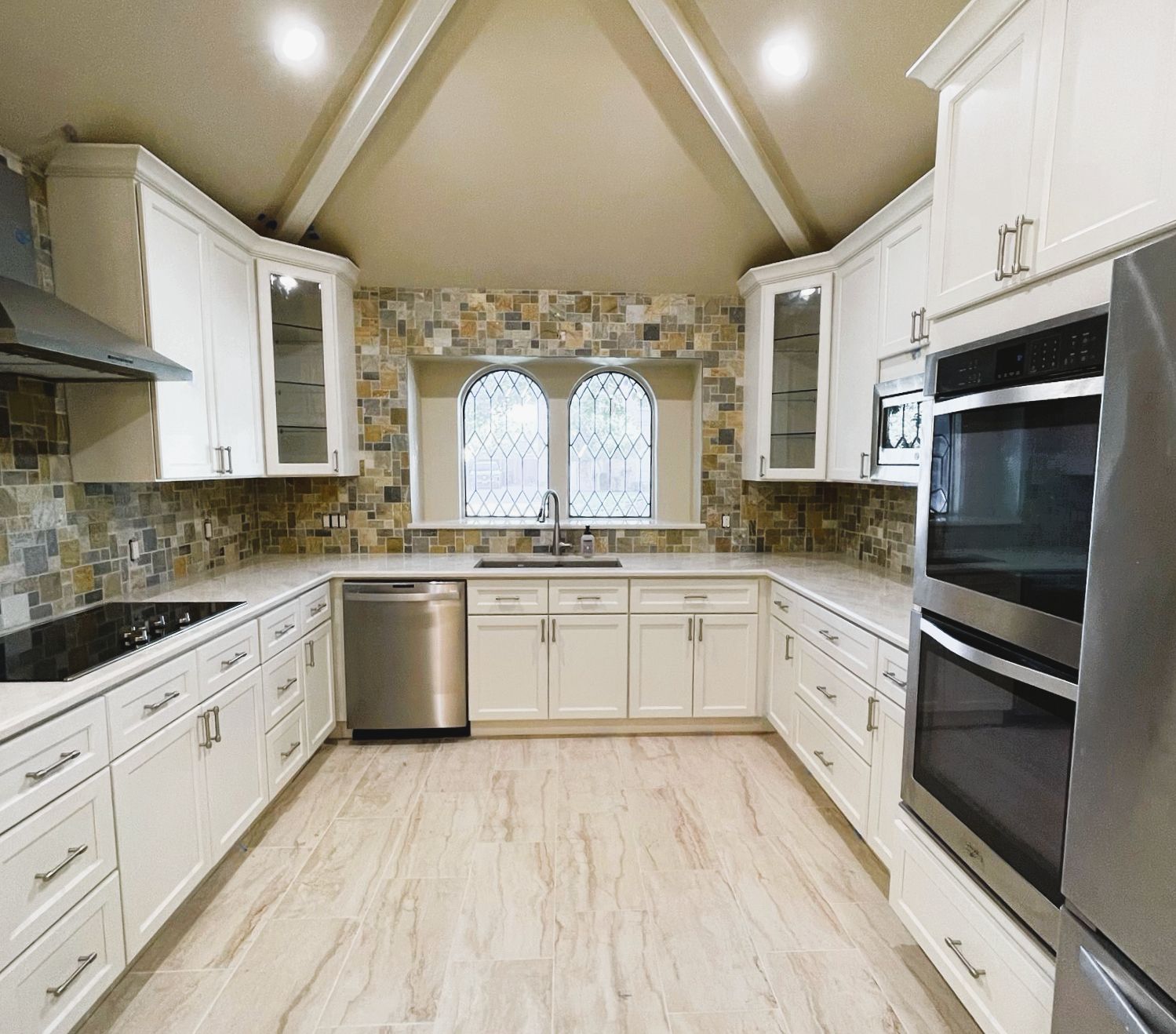 White kitchen with stainless steel appliances, stone backsplash, and arched window.