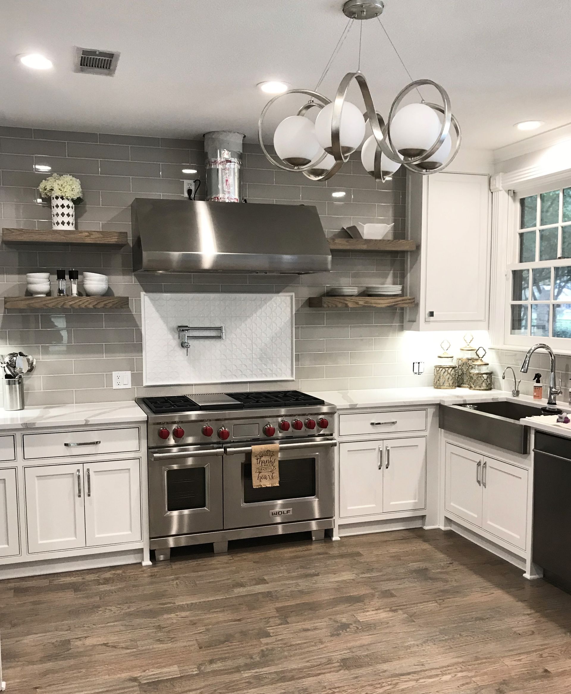 Stylish kitchen with stainless steel appliances, white cabinets, and floating wooden shelves.