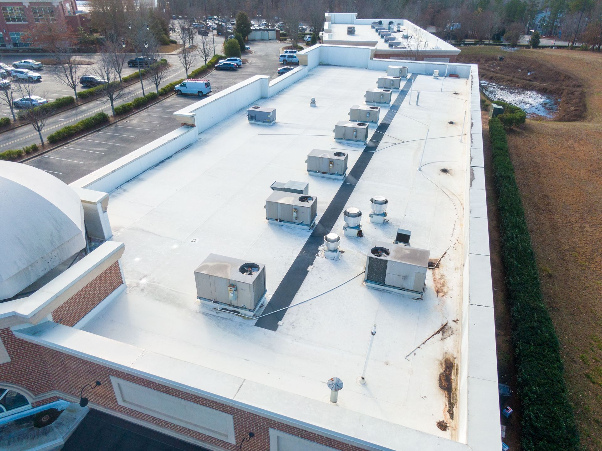Aerial view of a flat commercial roof with HVAC units. Cars parked in a lot are visible nearby.