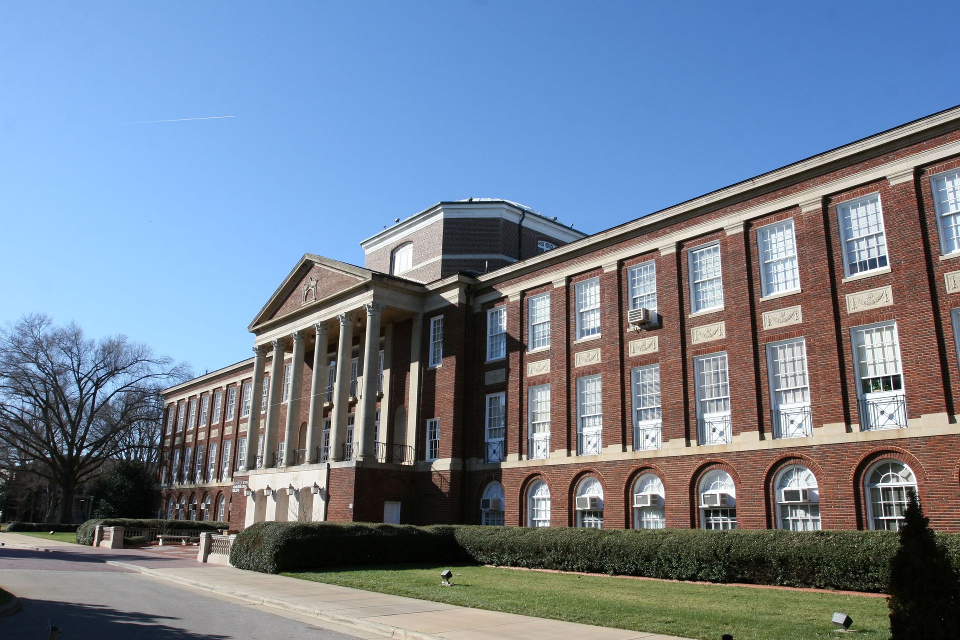 Brick building with white columns and windows under a clear, blue sky.