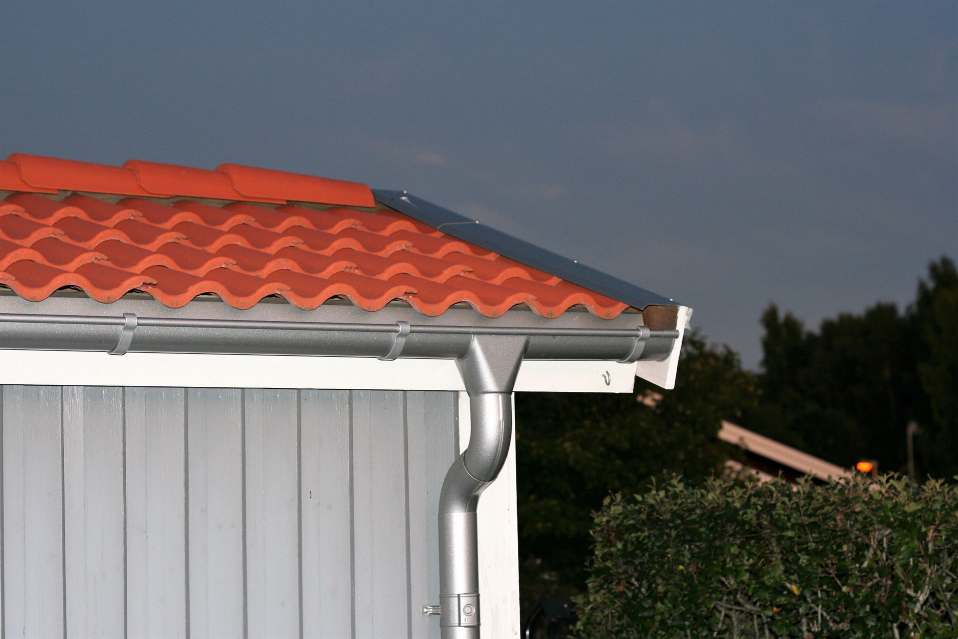Orange tiled roof with silver rain gutter on a white building.